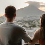 A young couple shares a romantic moment, overlooking Monterrey's cityscape and mountains at sunset.